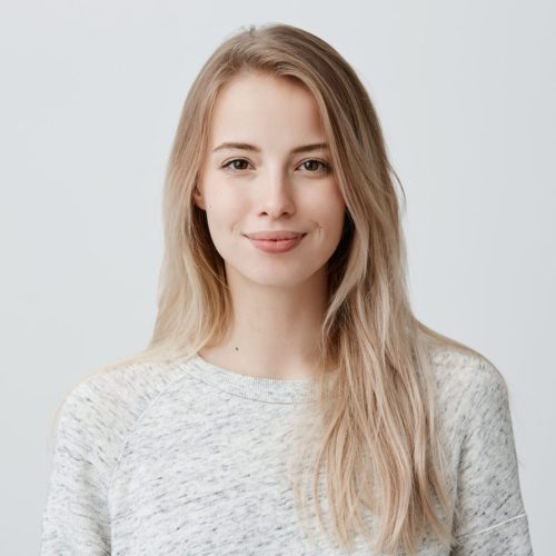 Pretty smiling joyfully female with fair hair, dressed casually, looking with satisfaction at camera, being happy. Studio shot of good-looking beautiful woman isolated against blank studio wall.